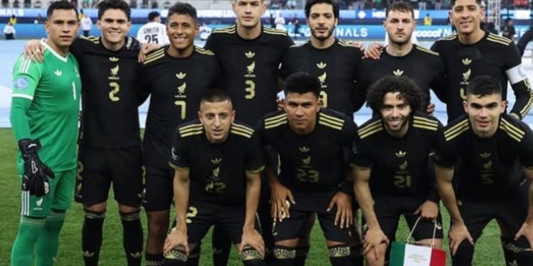 Jugadores de la Selección Mexicana 2025 concentrados en el campo durante un partido amistoso, con el estadio lleno de aficionados.