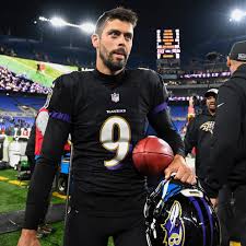 Justin Tucker sostiene balón y casco en la banca de los Ravens