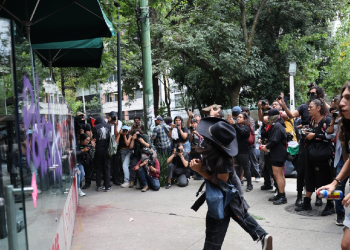 Manifestante realizando actos de vandalismo en un local comercial durante marcha contra la gentrificación