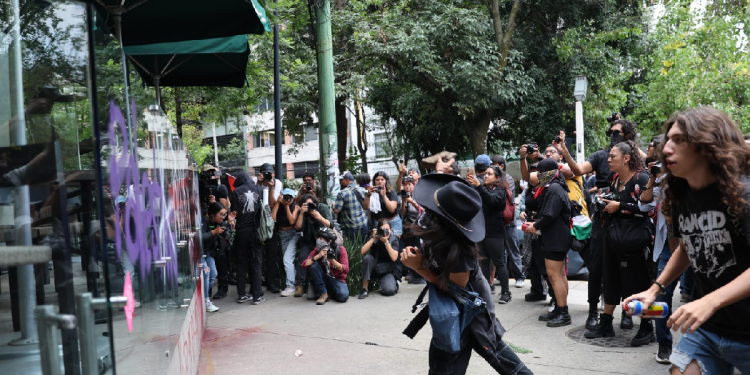Manifestante realizando actos de vandalismo en un local comercial durante marcha contra la gentrificación