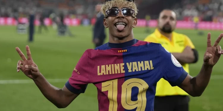 Lamine Yamal celebrando con la camiseta del Barcelona tras un partido, posando para la afición.