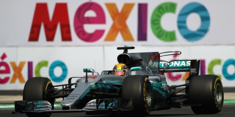 Monoplaza de Fórmula 1 compitiendo en el Autódromo Hermanos Rodríguez con el logo de México al fondo.