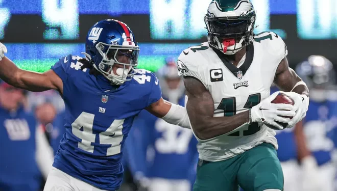 Defensivo de Giants intenta detener a receptor de Eagles en duelo divisional.